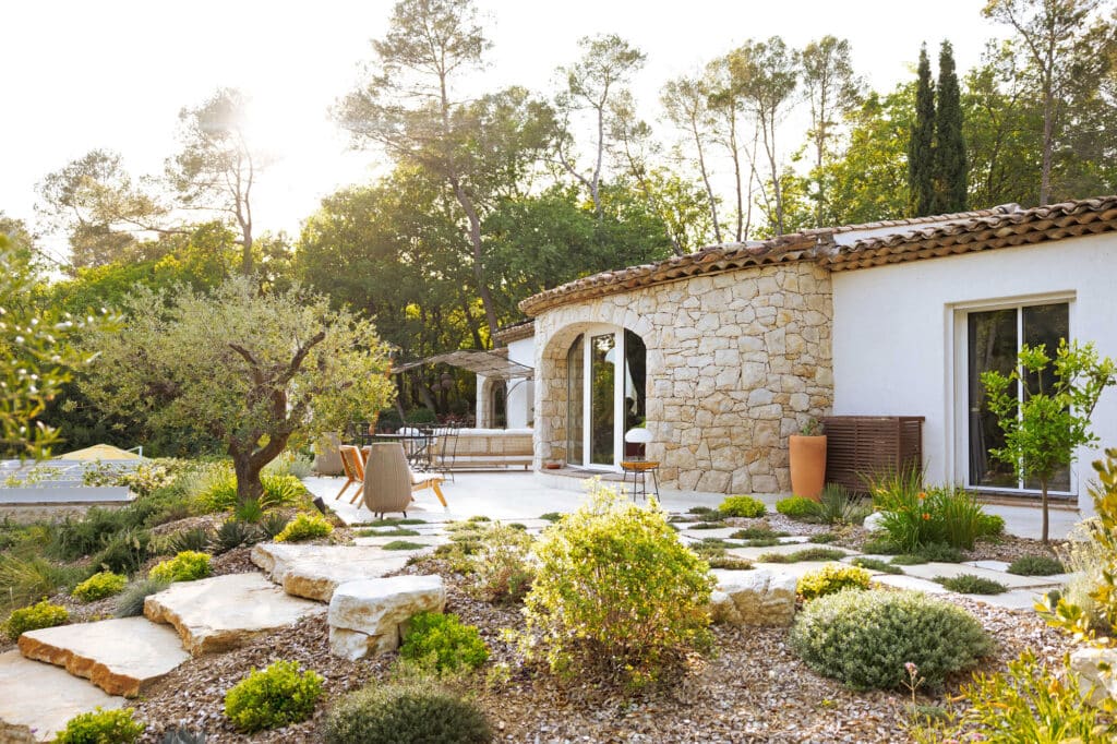 Jardin méditerranéen ensoleillé. Maison provençale, façade en pierre, terrasse, olivier et grandes dalles de pierre naturelles.