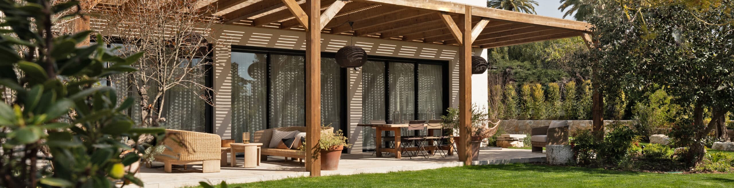 Terrasse jardin moderne sous pergola bois, ombrageant salon en rotin et table à manger. Aménagement extérieur luxueux et verdoyant.